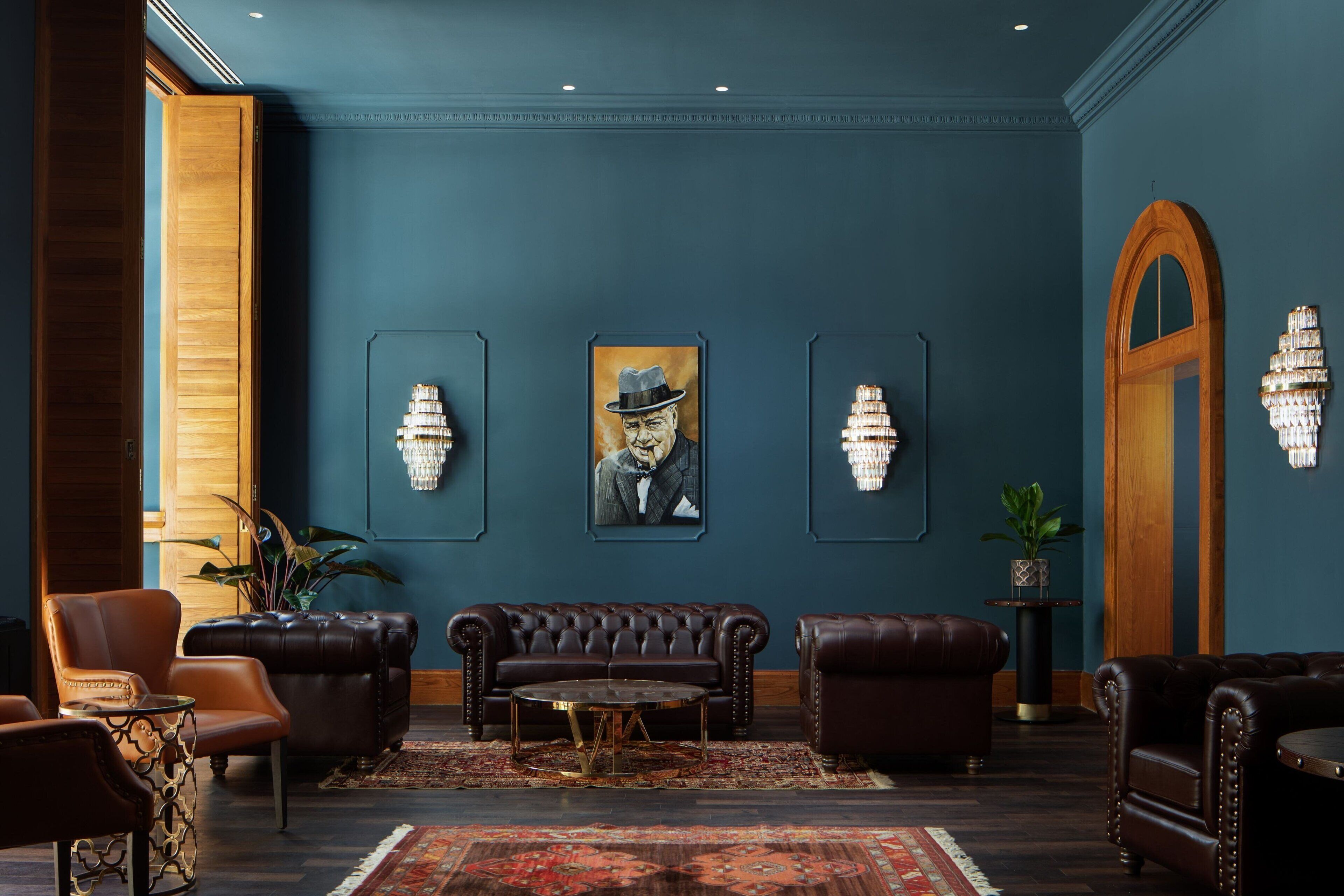 Un hall d’entrée aux murs bleu foncé, agrémenté d’un grand lustre et d’un canapé classique en cuir.
