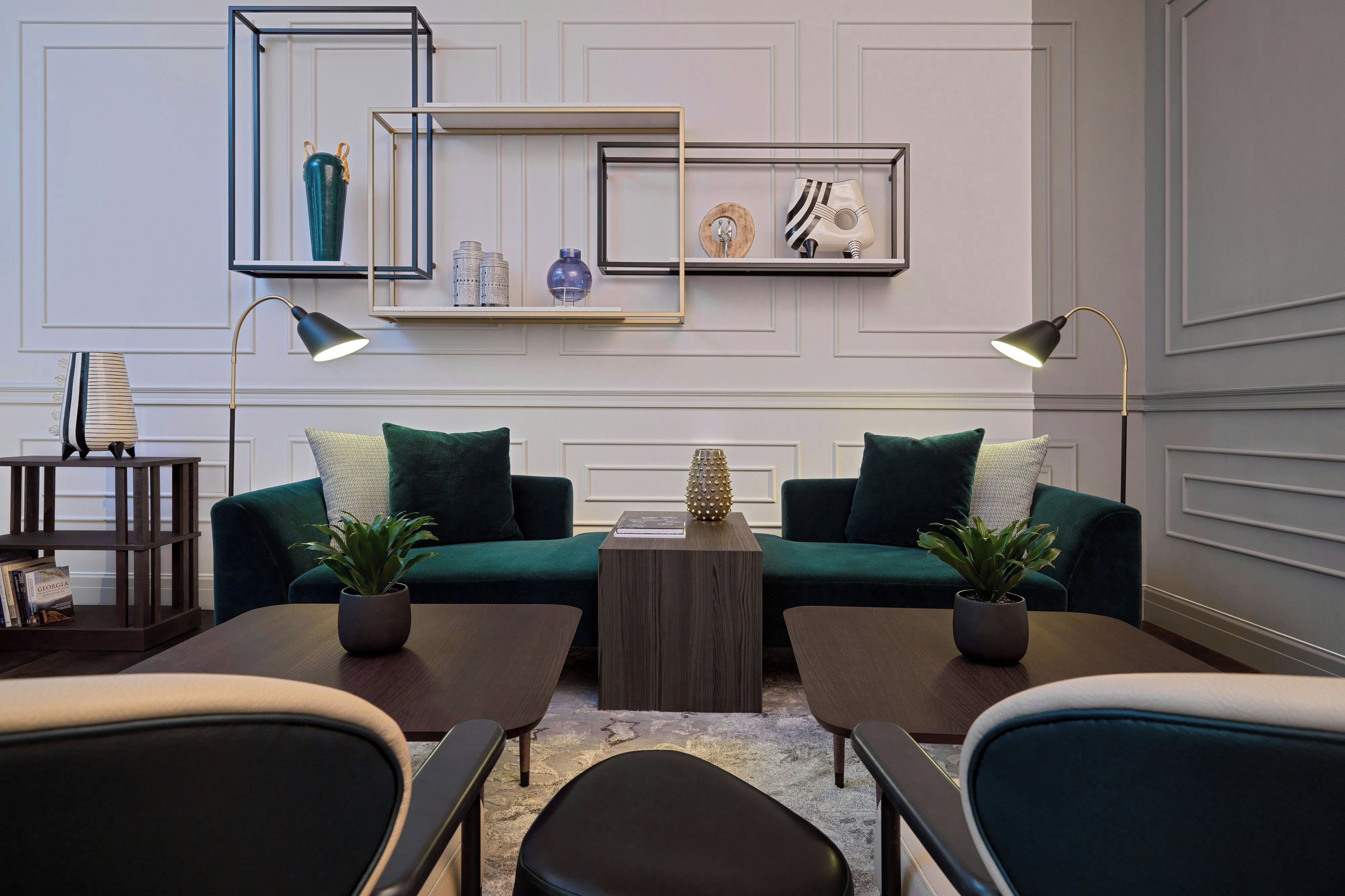A modern living room with a green sofa, two side tables, a coffee table, and decorative items on shelves.
