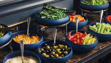 Une table de buffet avec divers aliments présentés dans des bols bleus, notamment des olives, du maïs et des légumes.