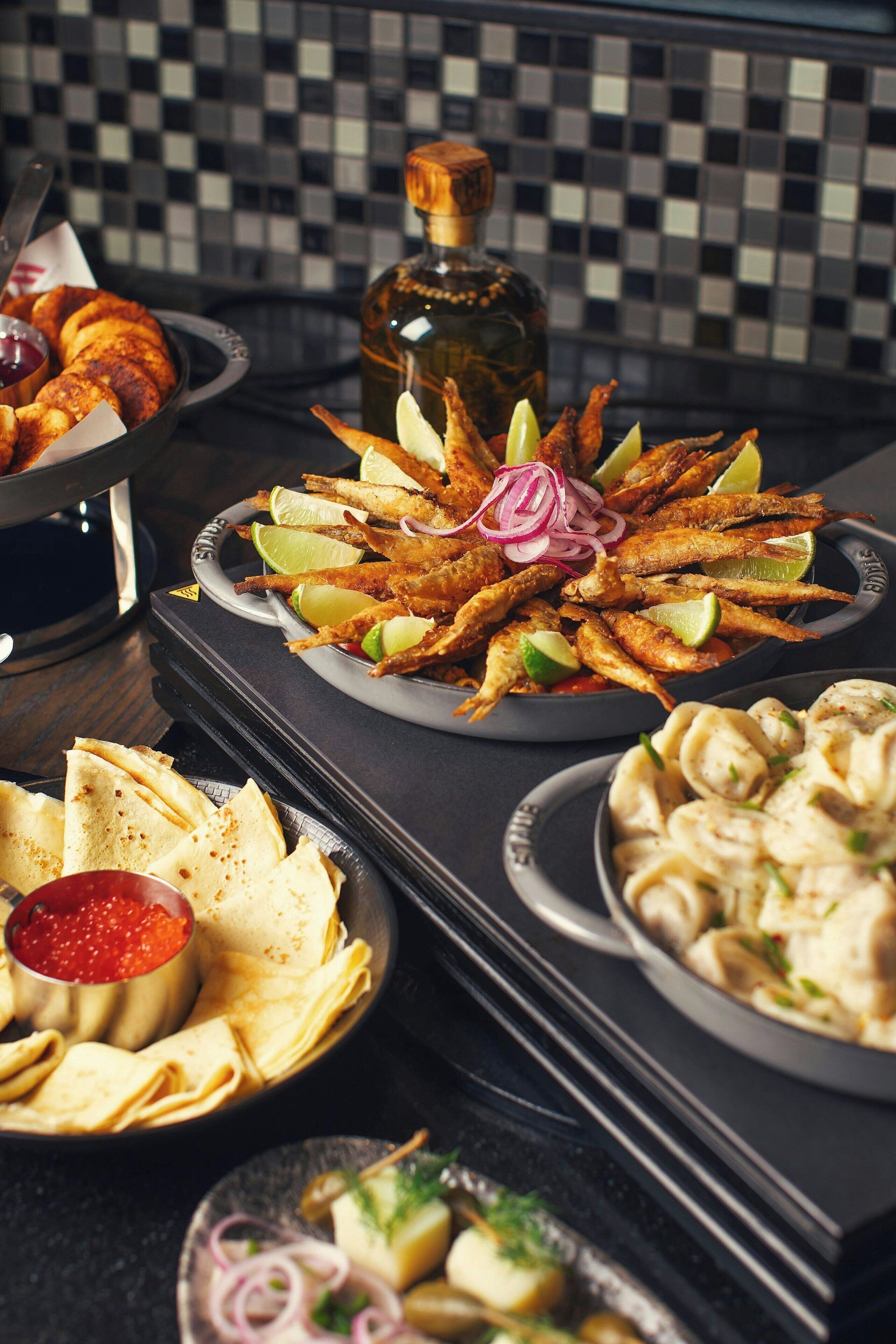 A table with various dishes including fried fish, tortillas, and a bottle of olive oil.