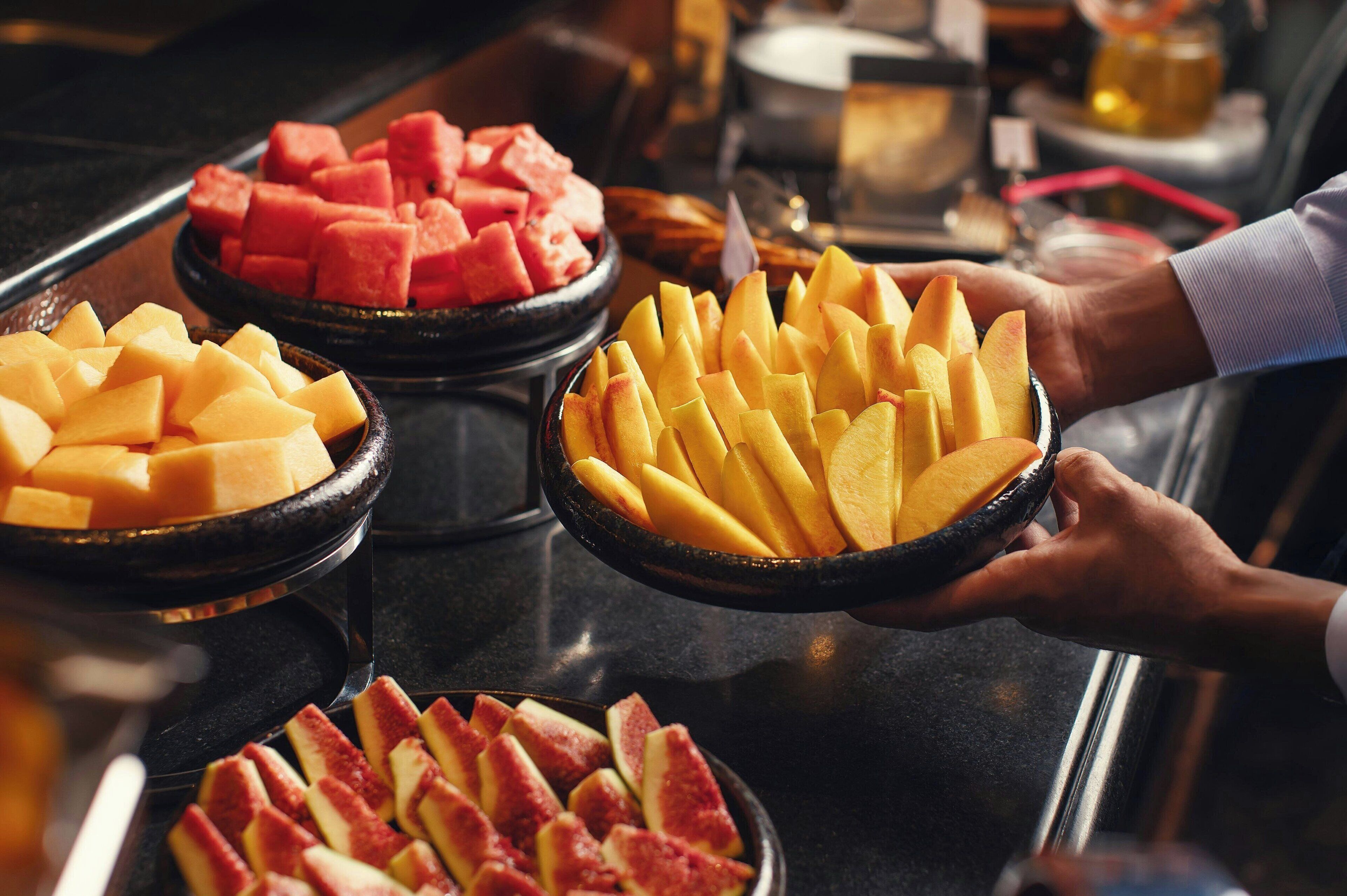 Un bufé con diversas frutas, como sandía, melón y manzanas rojas.