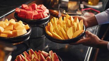 Un bufé con diversas frutas, como sandía, melón y manzanas rojas.