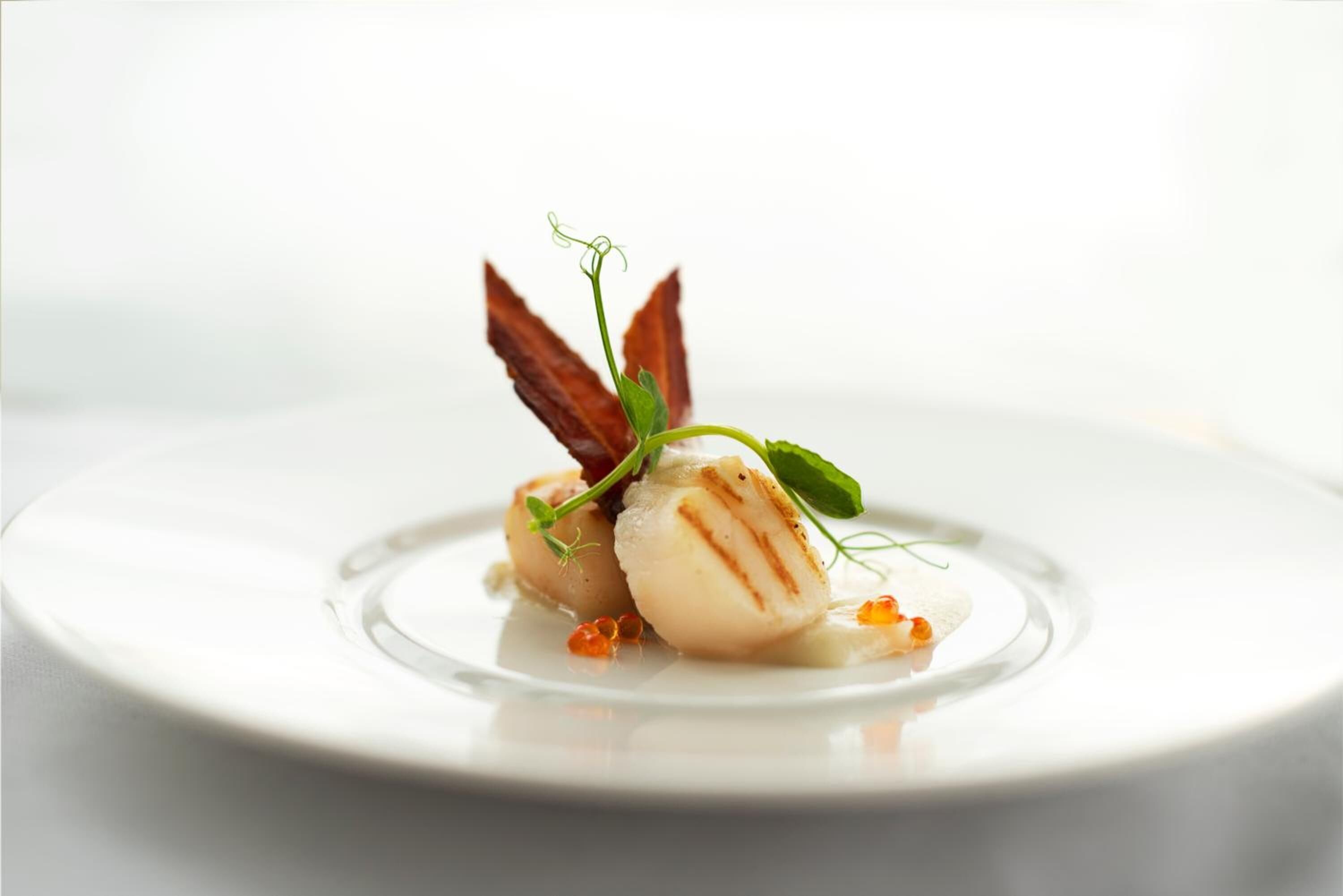 A plate with a food item, possibly a scallop, garnished with green herbs and a leaf.