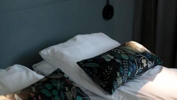 A neatly made bed with white linens and two decorative pillows, a wall-mounted light fixture, and a dark blue headboard.