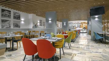 A modern dining area with multiple tables and chairs, a patterned floor, and a wooden ceiling.