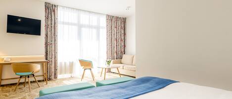 A hotel room with a bed, a desk, a chair, a sofa, and a TV.