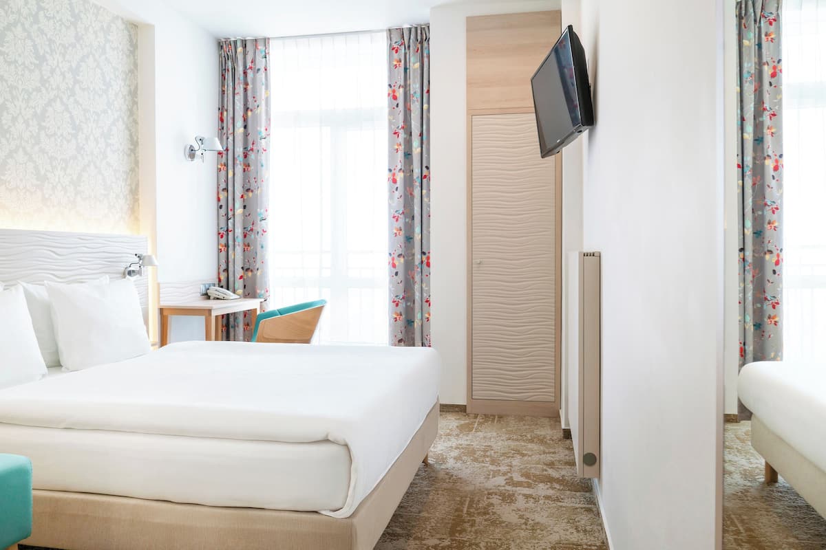 A hotel room with a bed, a desk, a chair, a television, and a wardrobe.