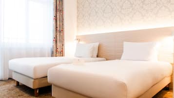 Een hotelkamer met twee bedden, behang met een patroon en een gordijn met een bloemenprint.