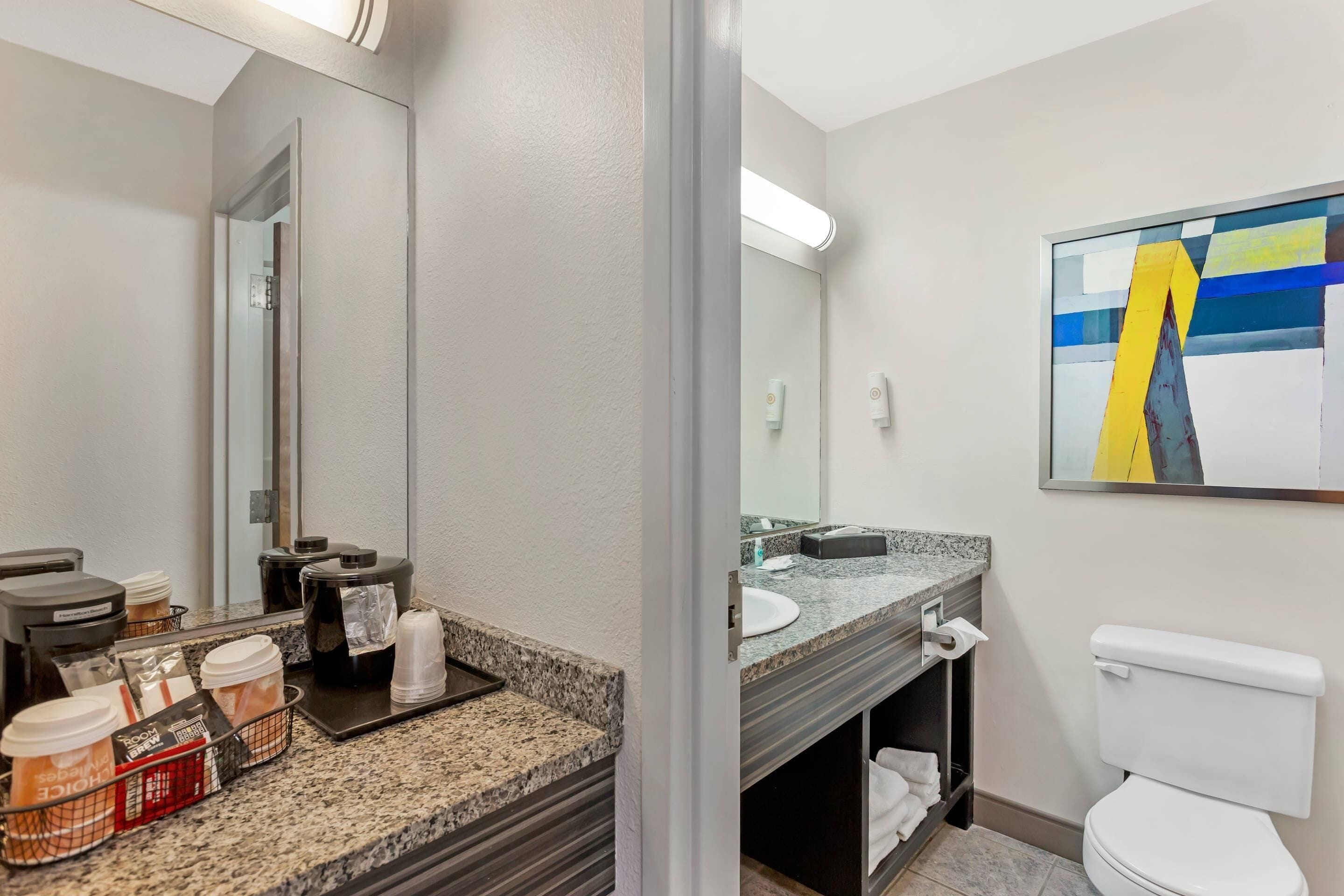 A modern bathroom with a granite countertop, a white toilet, and a large mirror.