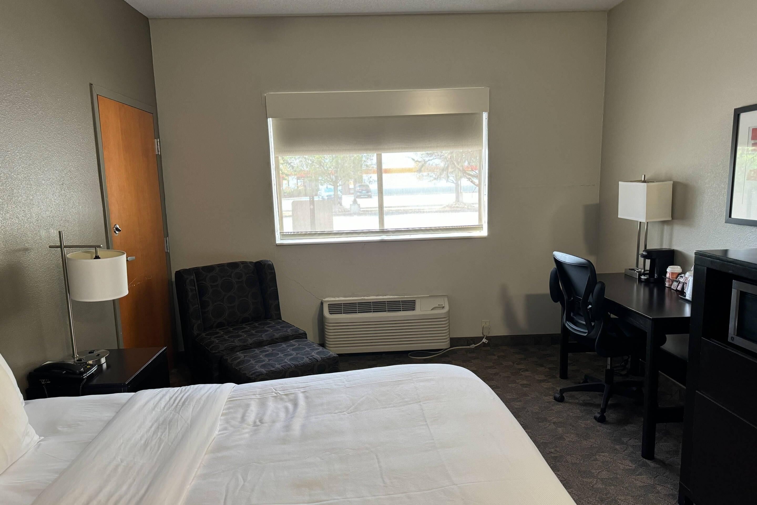 Een hotelkamer met een bed, een bureau, een stoel, een bureaulamp, een verwarming en een raam met uitzicht.