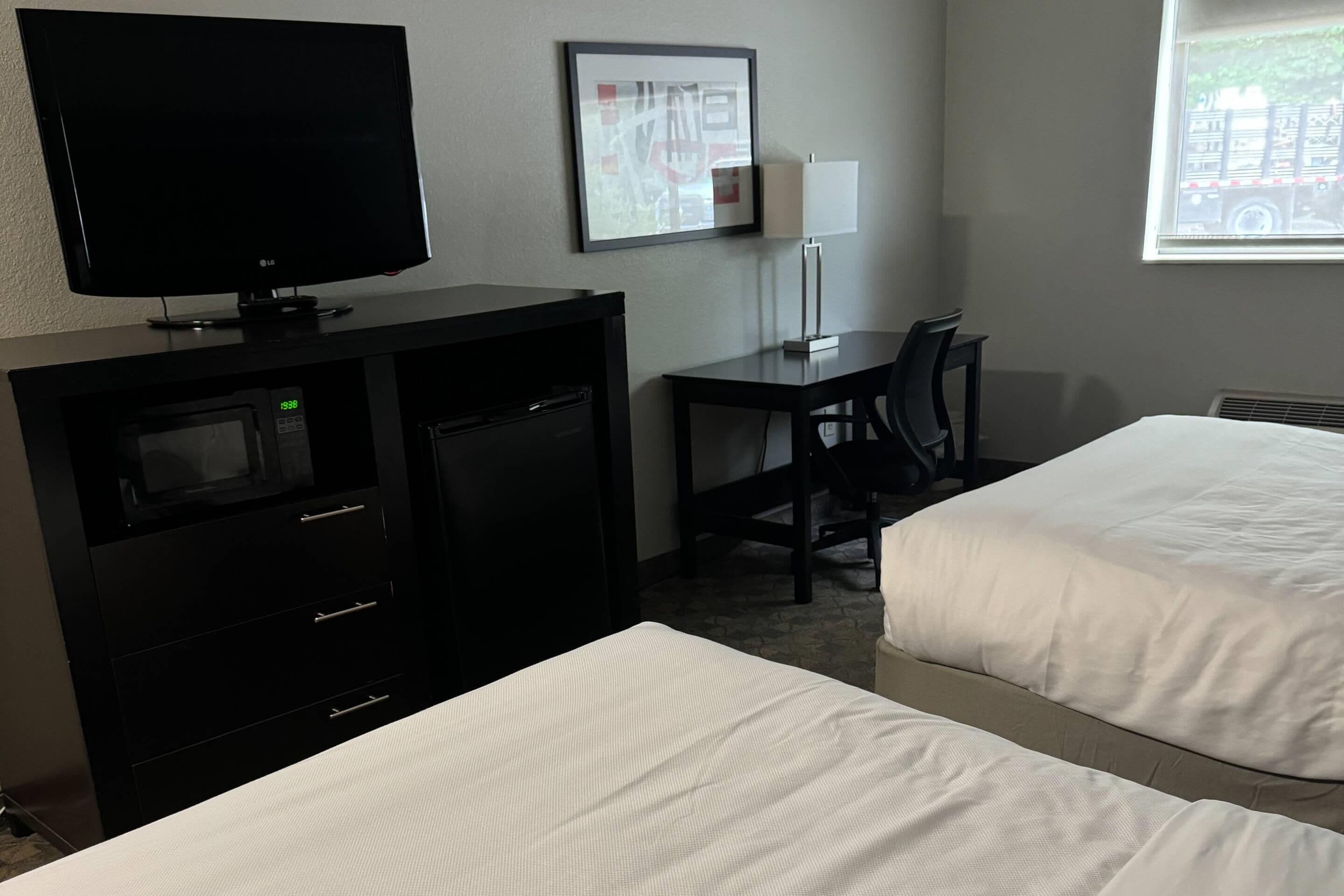 A hotel room with a TV, desk, chair, two beds, and a window with a view of a truck.