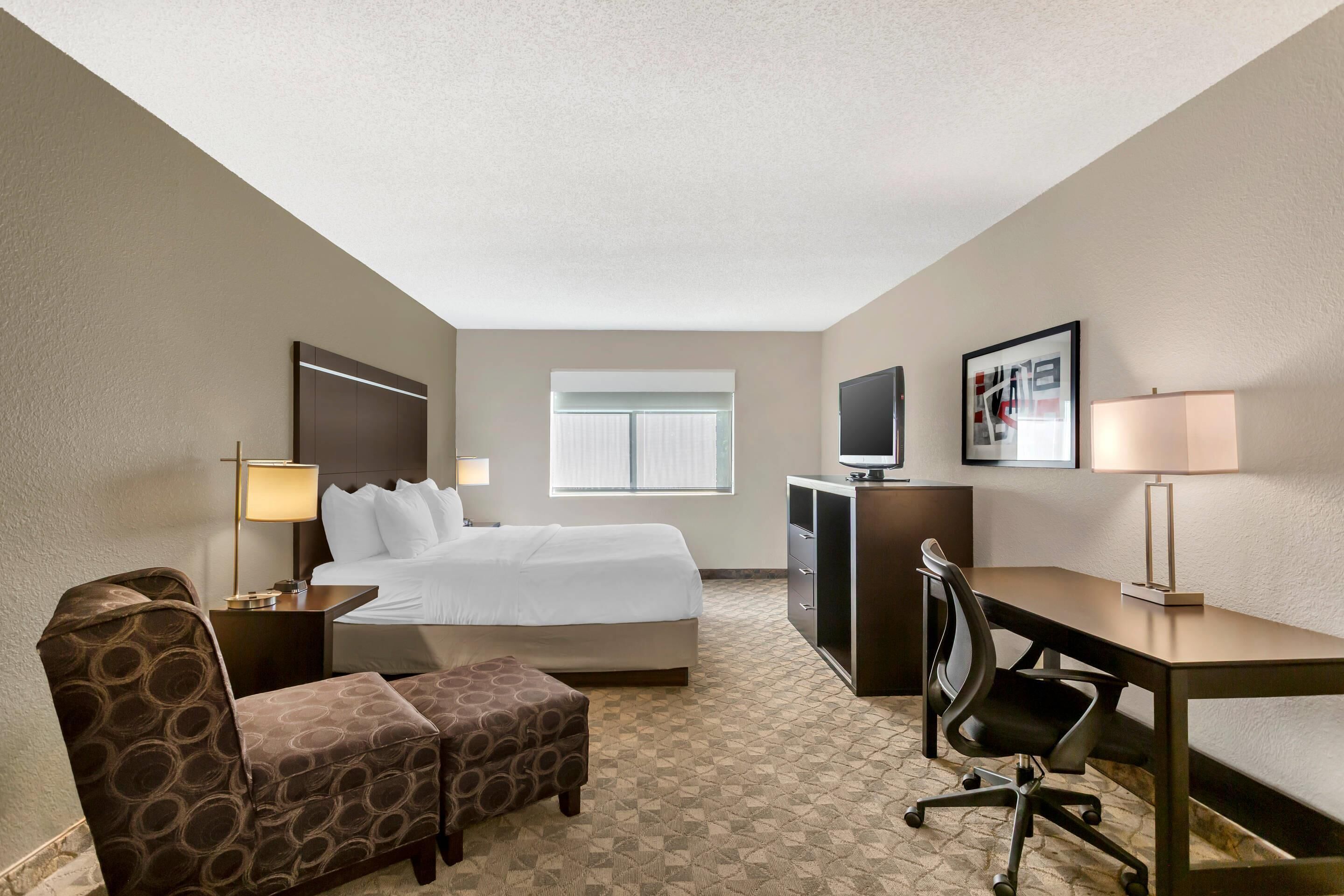 Une chambre d’hôtel avec un lit, un bureau, une chaise, une télévision, une lampe et une fenêtre.
