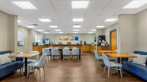 A spacious dining area with multiple tables and chairs, a kitchen in the background, and a blue sofa on the left. - Comfort Inn Huntington near University area (Huntington)