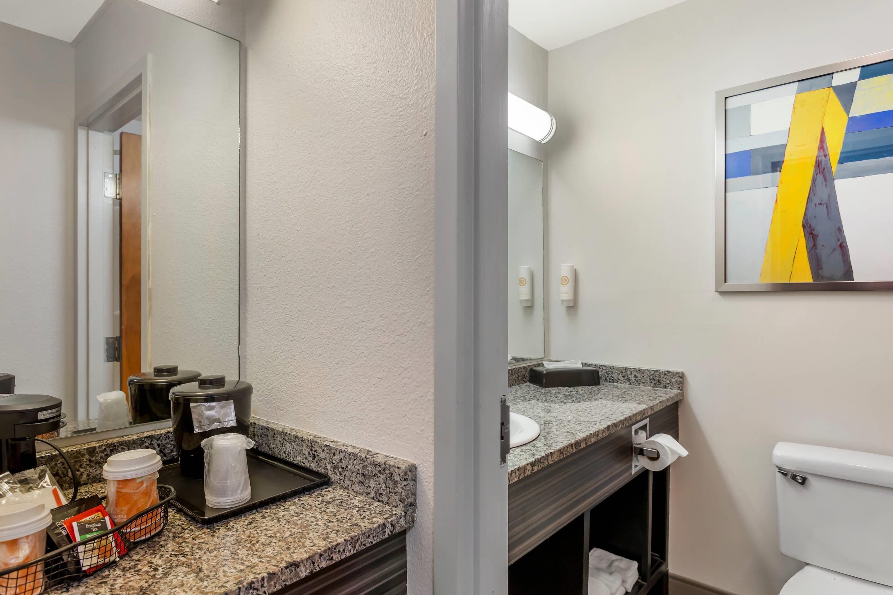 Un baño moderno con encimera de granito, cafetera y lavabo.