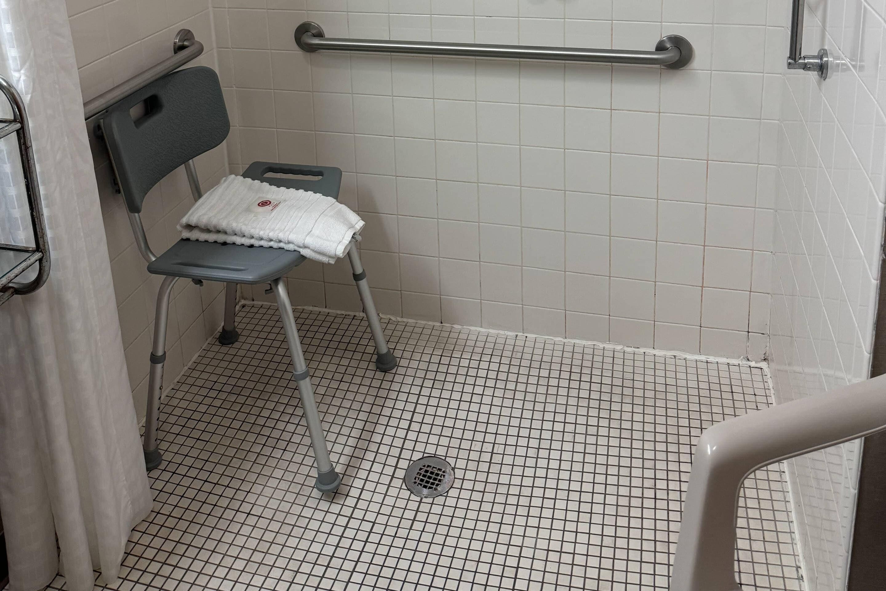 Baño con cabina de ducha accesible para sillas de ruedas, barra de apoyo y piso de baldosas.