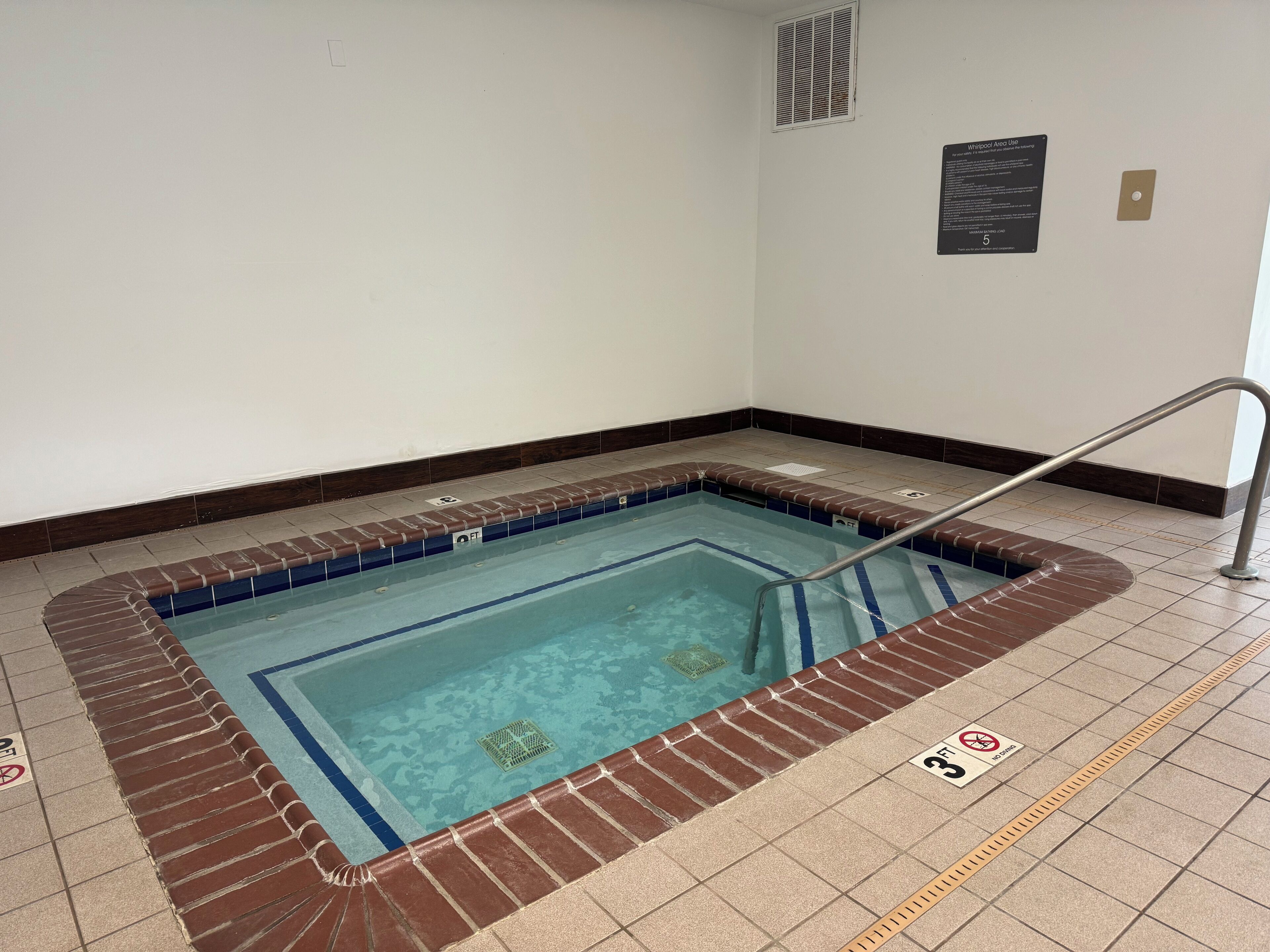 A swimming pool with a safety railing, a sign indicating no diving, and a Whirlpool area use sign.