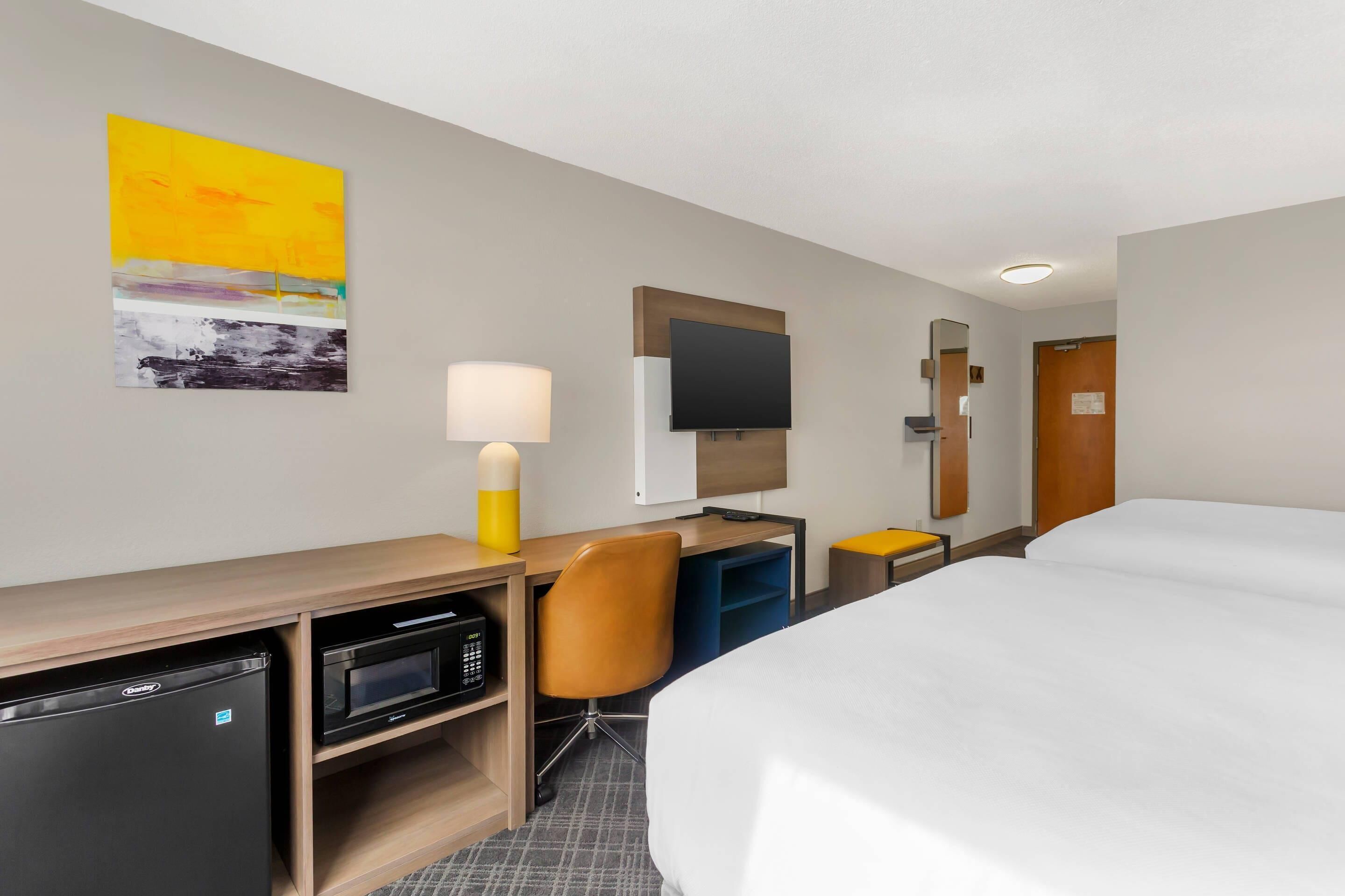 A hotel room with a bed, desk, microwave, and a television on the wall.