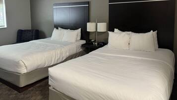 A hotel room with two beds, a nightstand with lamps, and a chair.