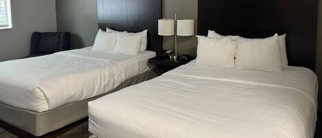 A hotel room with two beds, a nightstand with lamps, and a chair.