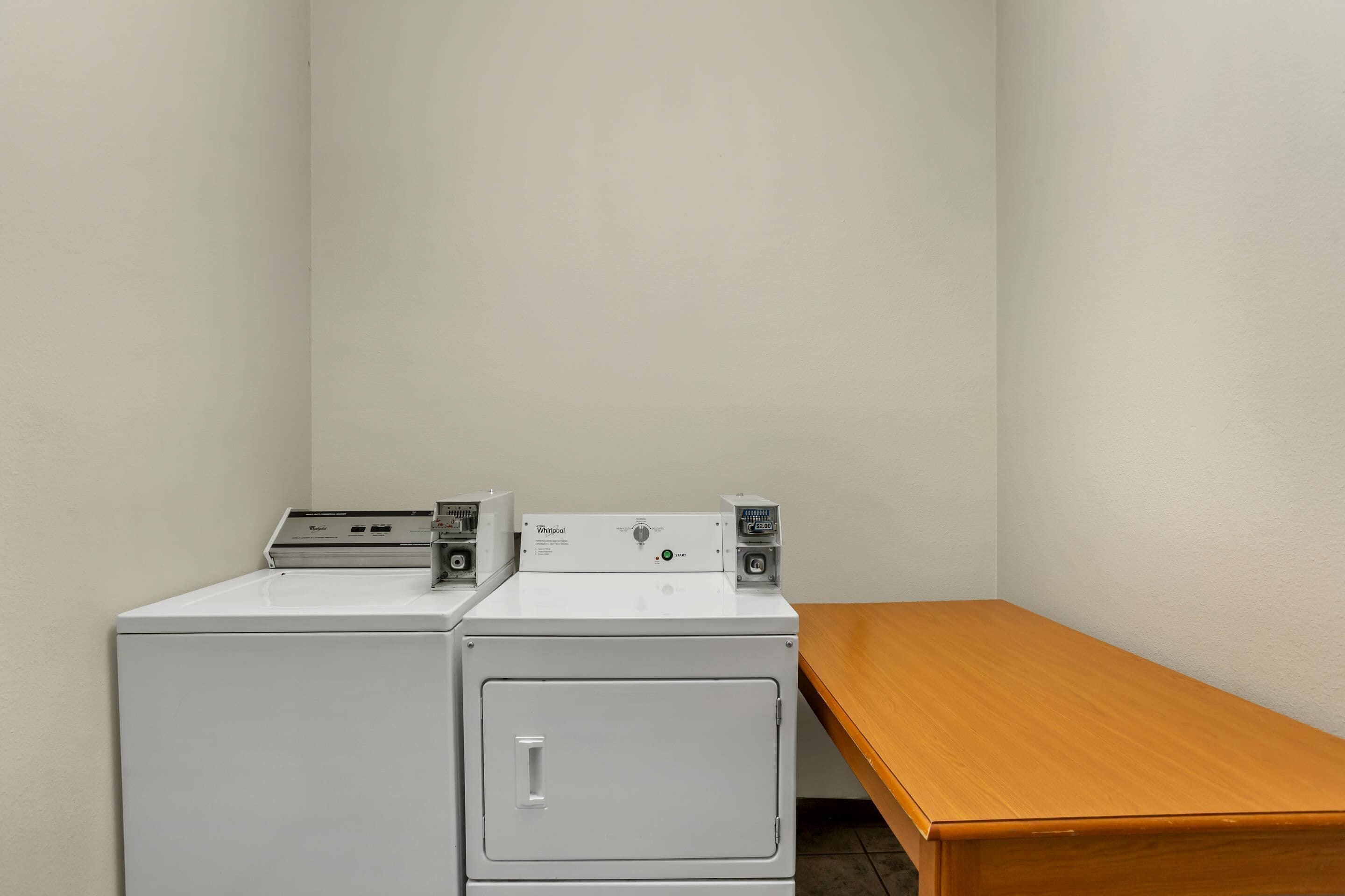 A laundry room with two stacked washers and dryers, a wooden bench, and a plain wall.
