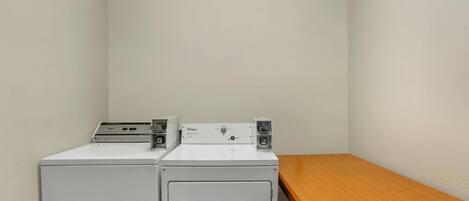 A laundry room with two stacked washers and dryers, a wooden bench, and a plain wall.