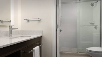 Un baño moderno con cabina de ducha de vidrio, un lavabo blanco con grifo cromado y un mueble de tocador de madera oscura.