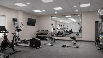A gym with exercise equipment, a large mirror, and a wall-mounted TV.