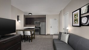 A modern living room with a flat-screen TV, a grey sofa, and a dining area with a table and chairs. - Residence Inn by Marriott Charlotte SouthPark (Charlotte)