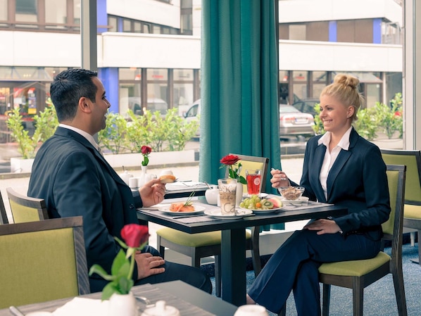 A man and a woman dining at a table with a view of the street, a rose, and a menu. - Mercure Hotel Frankfurt Eschborn Sued (Eschborn)