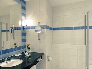 Ein Badezimmer mit Waschbecken, Spiegel, Handtuchhalter und Duschbereich.