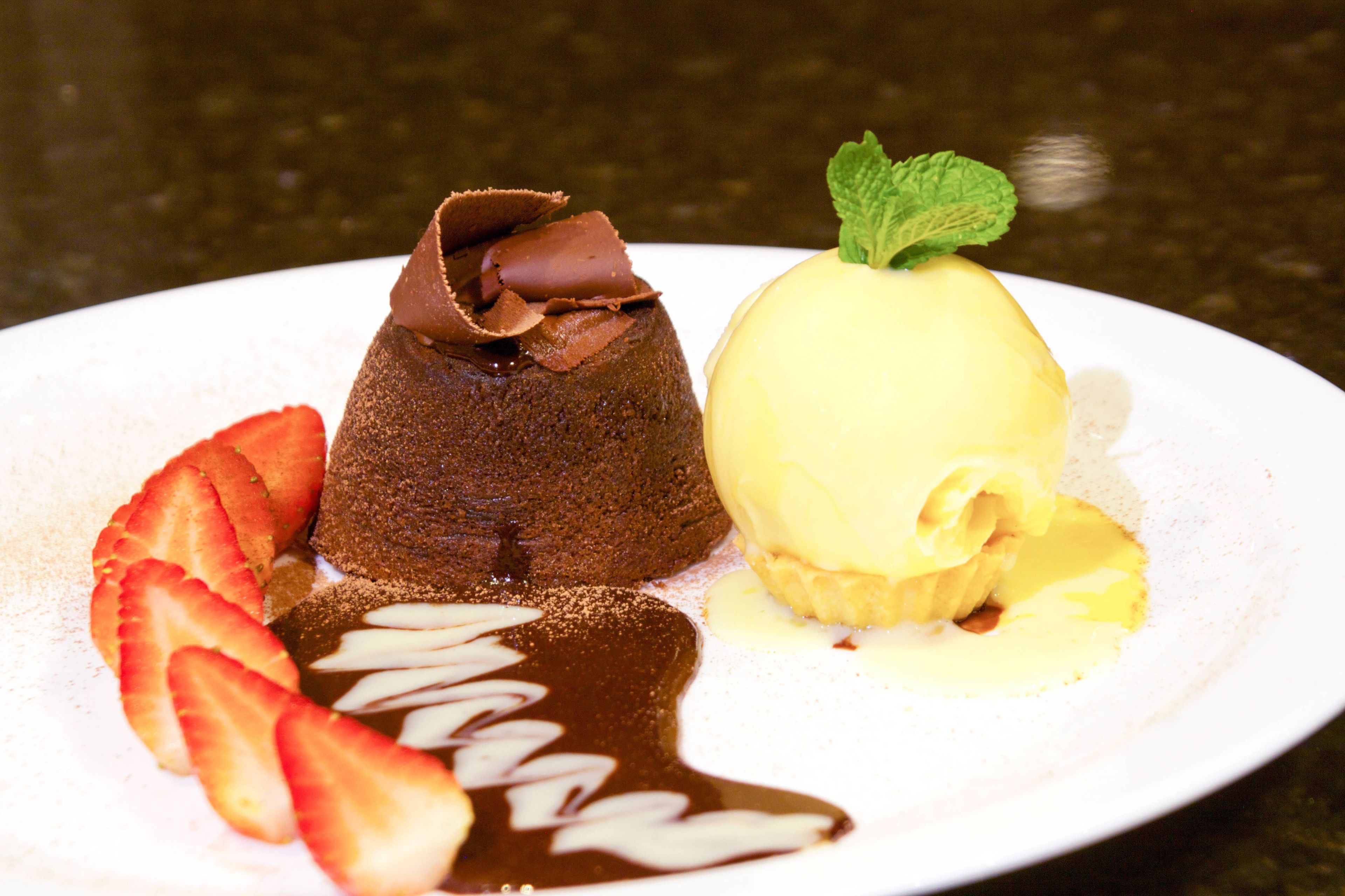 A dessert plate with chocolate lava cake, vanilla ice cream, strawberries, and chocolate sauce.