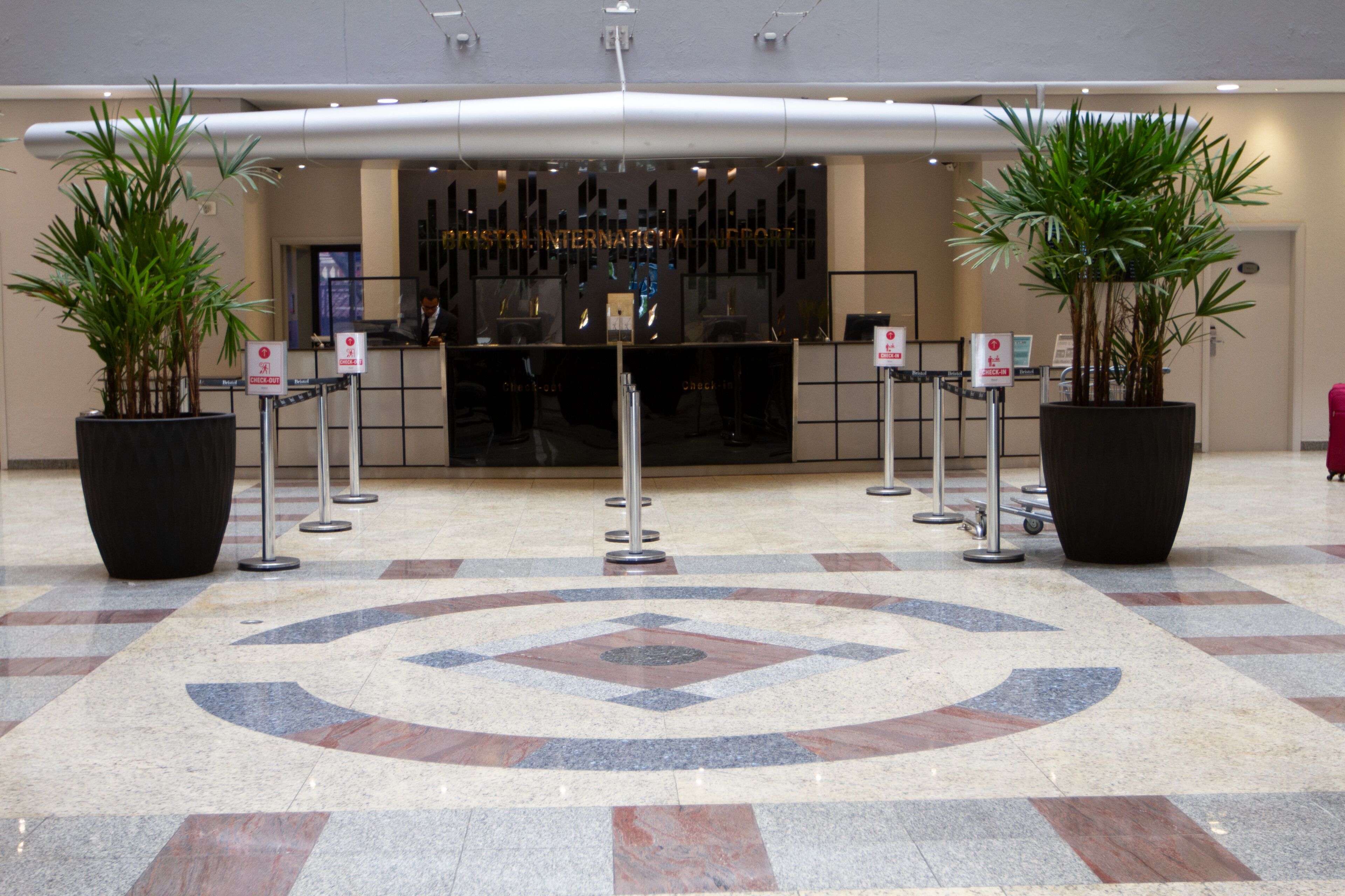 A reception area with a check-in counter, potted plants, and a tiled floor with a geometric pattern.