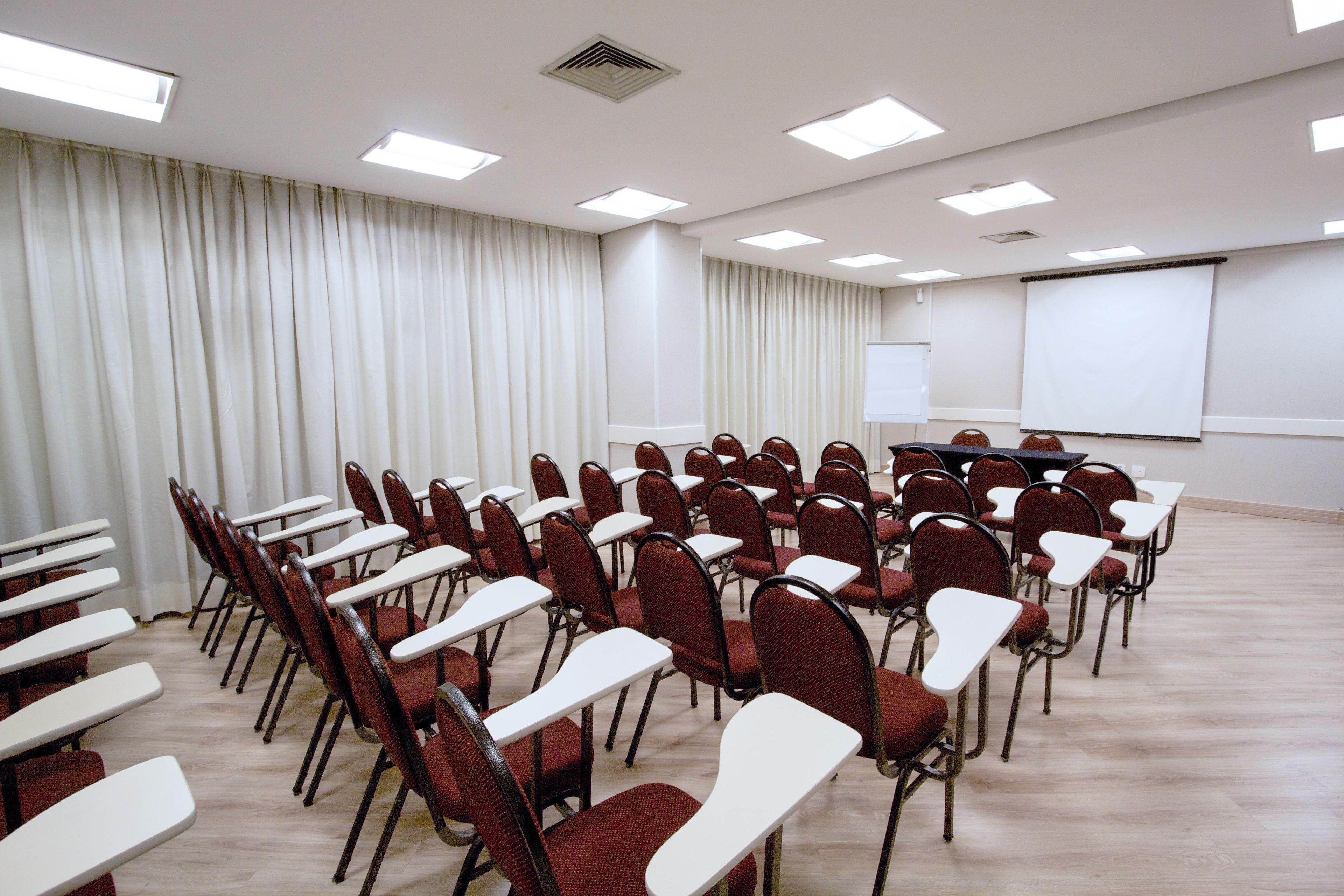 A conference room with rows of chairs, a projector screen, and a whiteboard.
