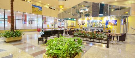 A spacious lobby with a piano, seating areas, and potted plants.