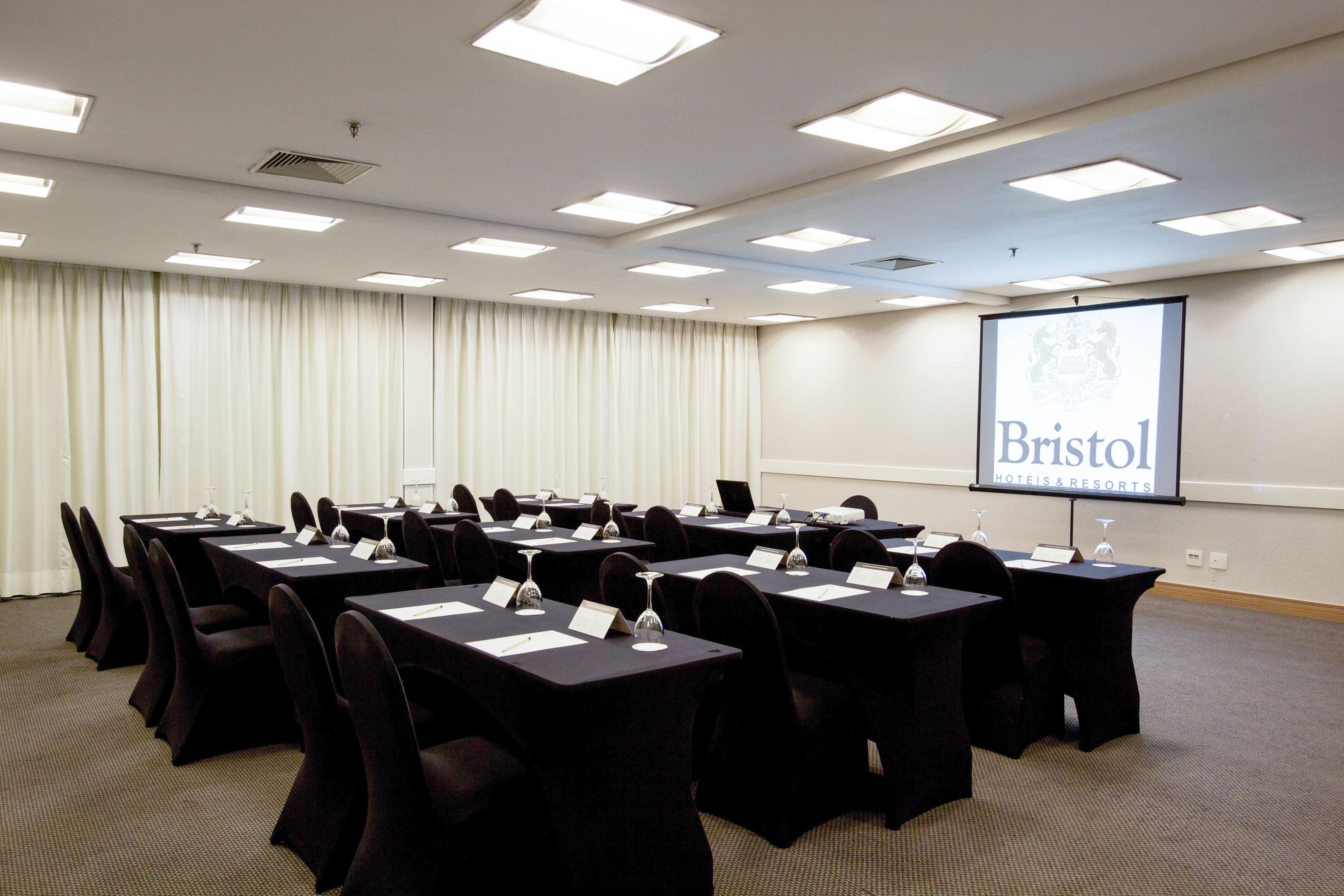 A conference room with tables, chairs, and a projector screen displaying 'Bristol Hotels & Resorts'.