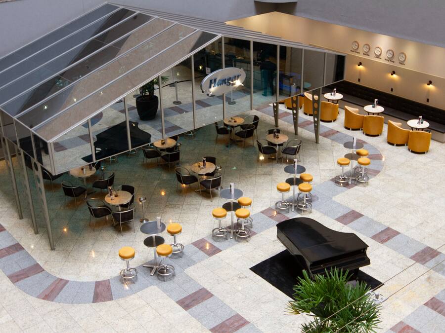 A spacious indoor area with multiple tables and chairs, a piano, and a glass-enclosed section.