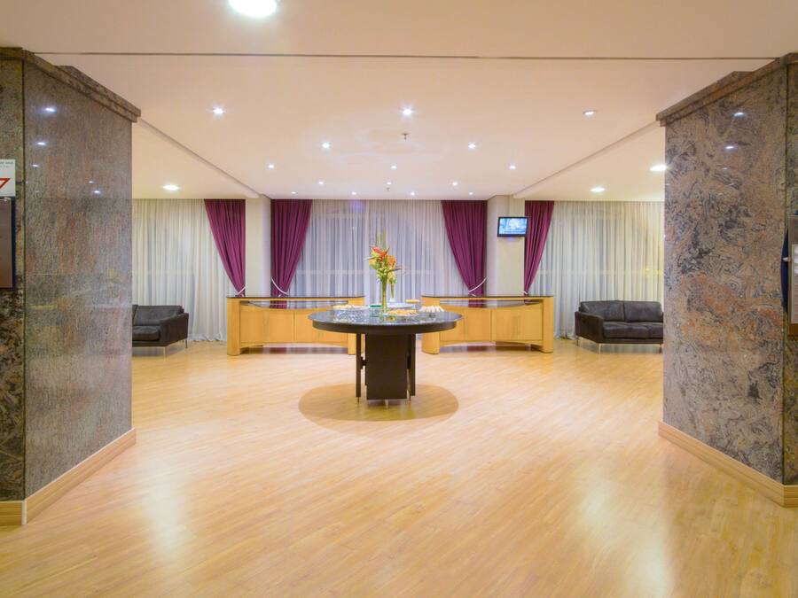 A spacious lobby with a central round table, two sofas, and a TV screen on the wall.