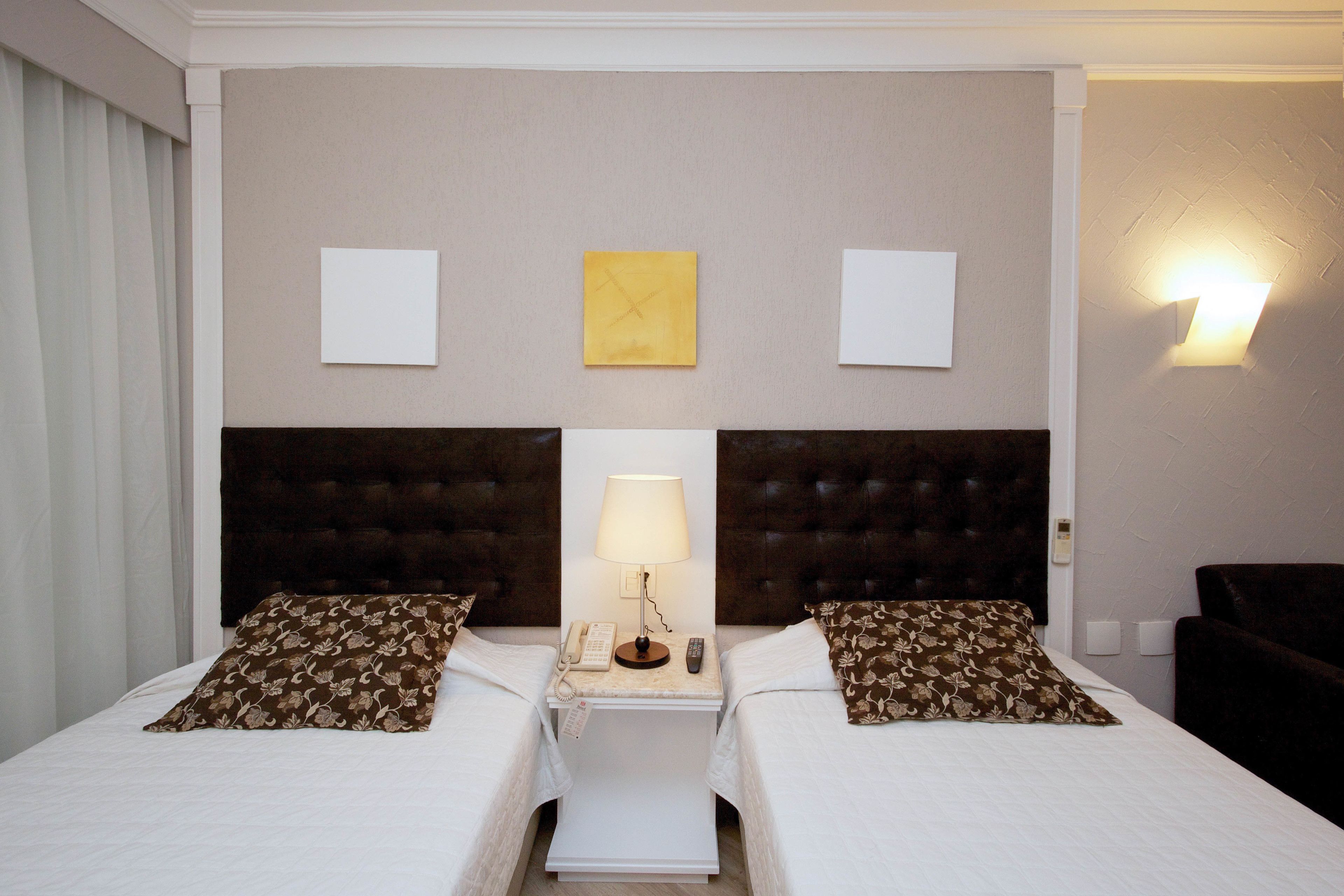 Een hotelkamer met twee bedden, een nachtkastje met een lamp, een telefoon en een wandlamp.