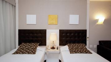 Een hotelkamer met twee bedden, een nachtkastje met een lamp, een telefoon en een wandlamp.