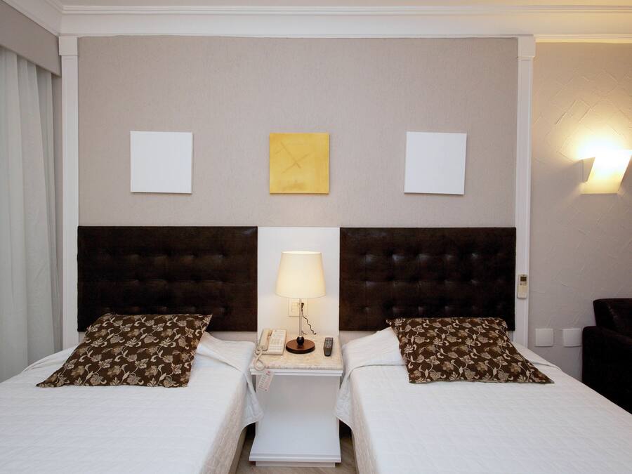 Een hotelkamer met twee bedden, een nachtkastje met een lamp, een telefoon en een wandlamp.
