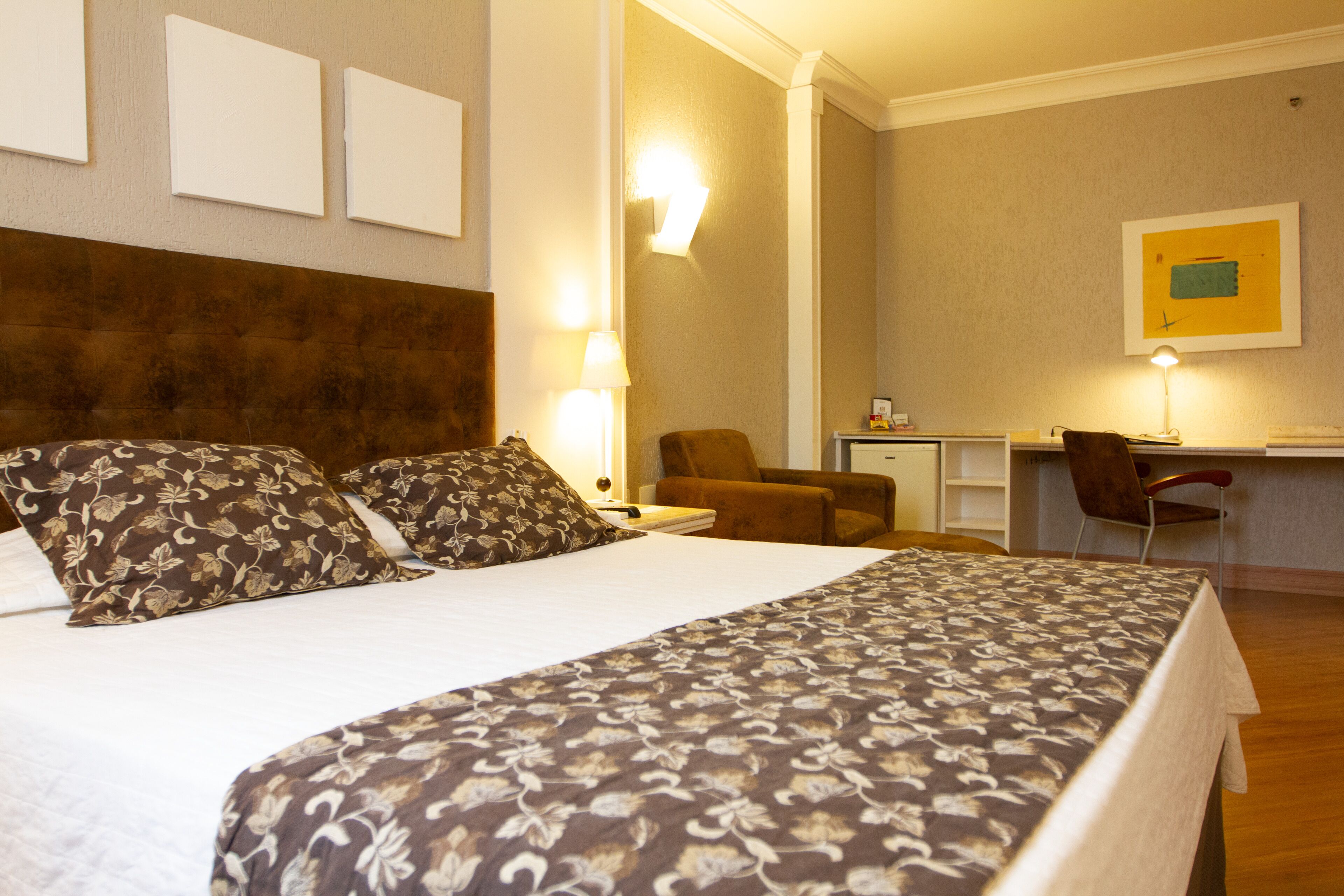 Una habitación de hotel con una cama grande, un escritorio, una silla y una lámpara.