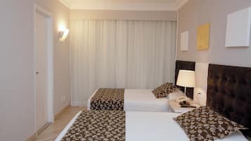 Quarto de hotel com duas camas, uma mesa de cabeceira com luminária, telefone e iluminação na parede.