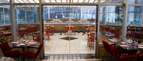 Un restaurante con fachada de vidrio, sillas rojas y mesas dispuestas para comer.