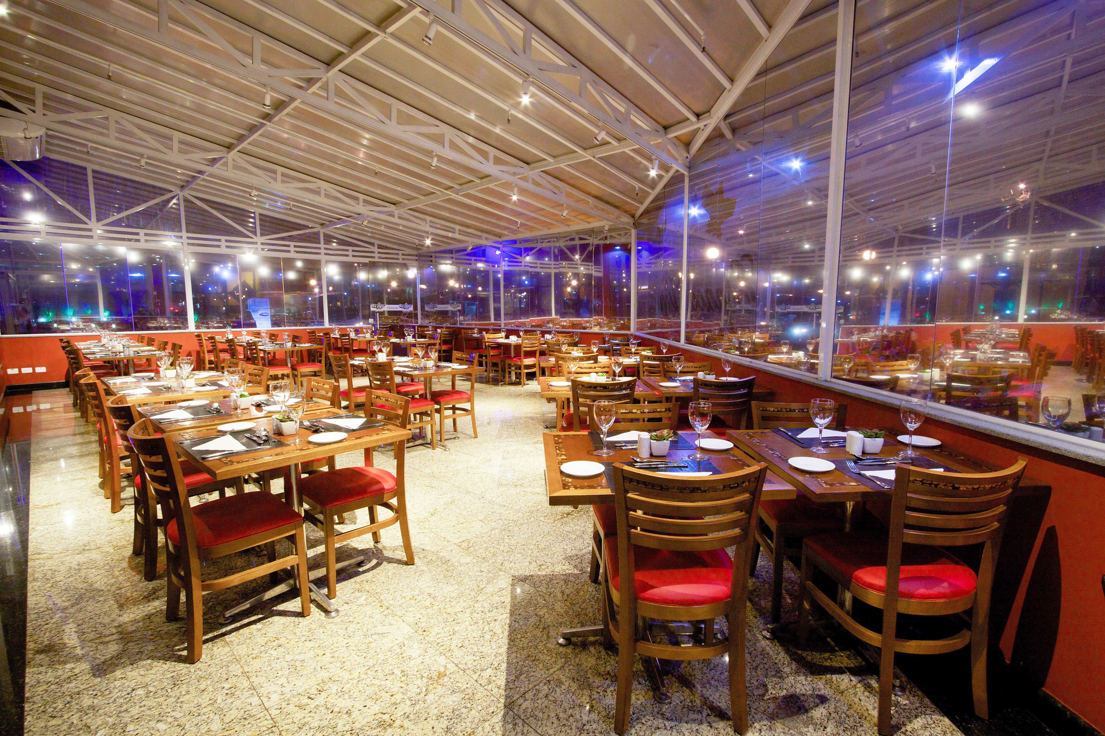 Un restaurante espacioso con numerosas mesas y sillas, ventanas amplias y un techo alto.