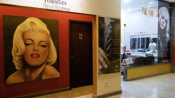 Corredor de hotel com placa de banheiro, uma porta e um grande cartaz de uma mulher.