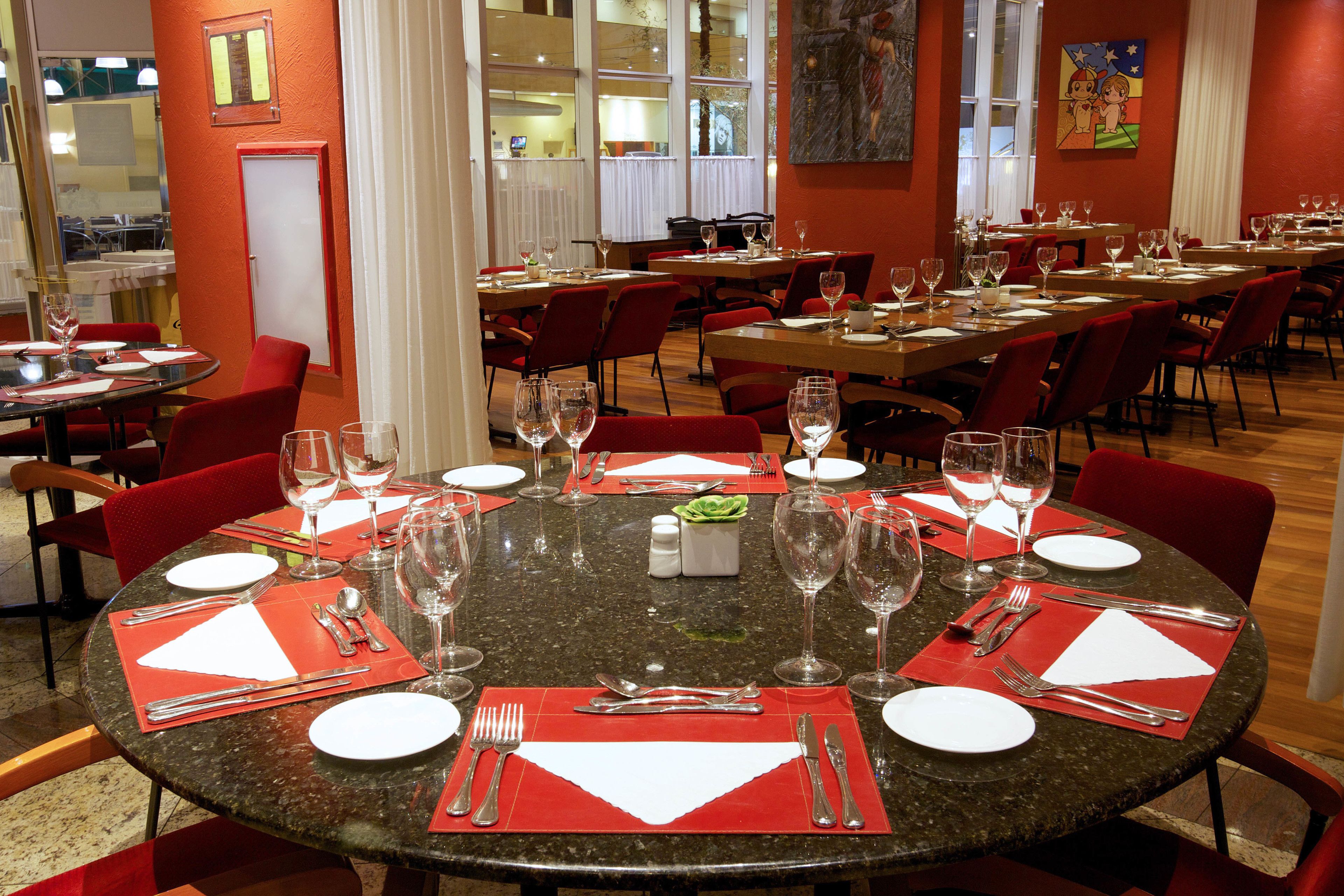 A restaurant with multiple dining tables set with red placemats, silverware, and wine glasses.
