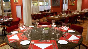 A restaurant with multiple dining tables set with red placemats, silverware, and wine glasses.