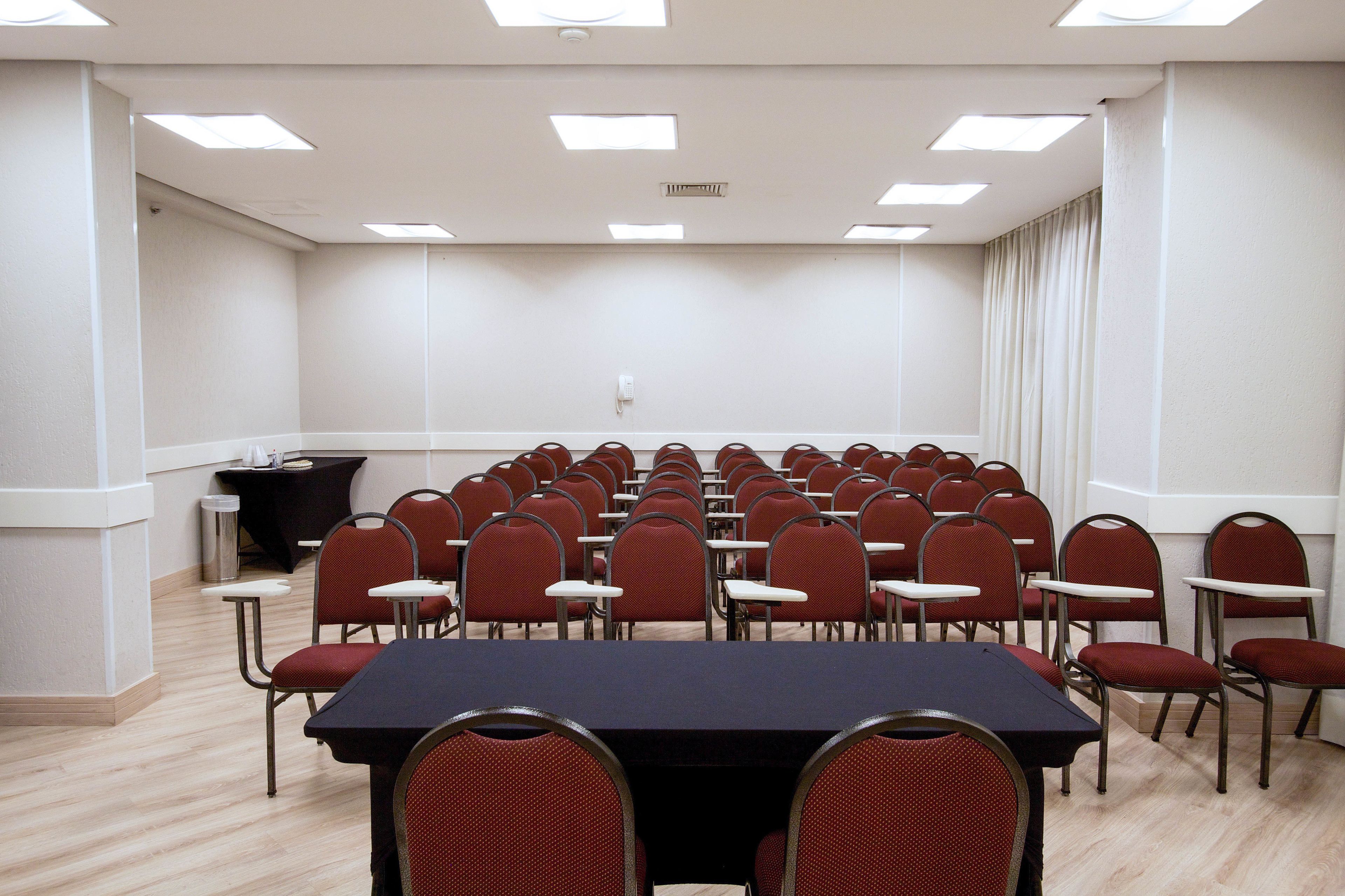 A conference room with a long table and multiple chairs, equipped with ceiling lights and a black podium.