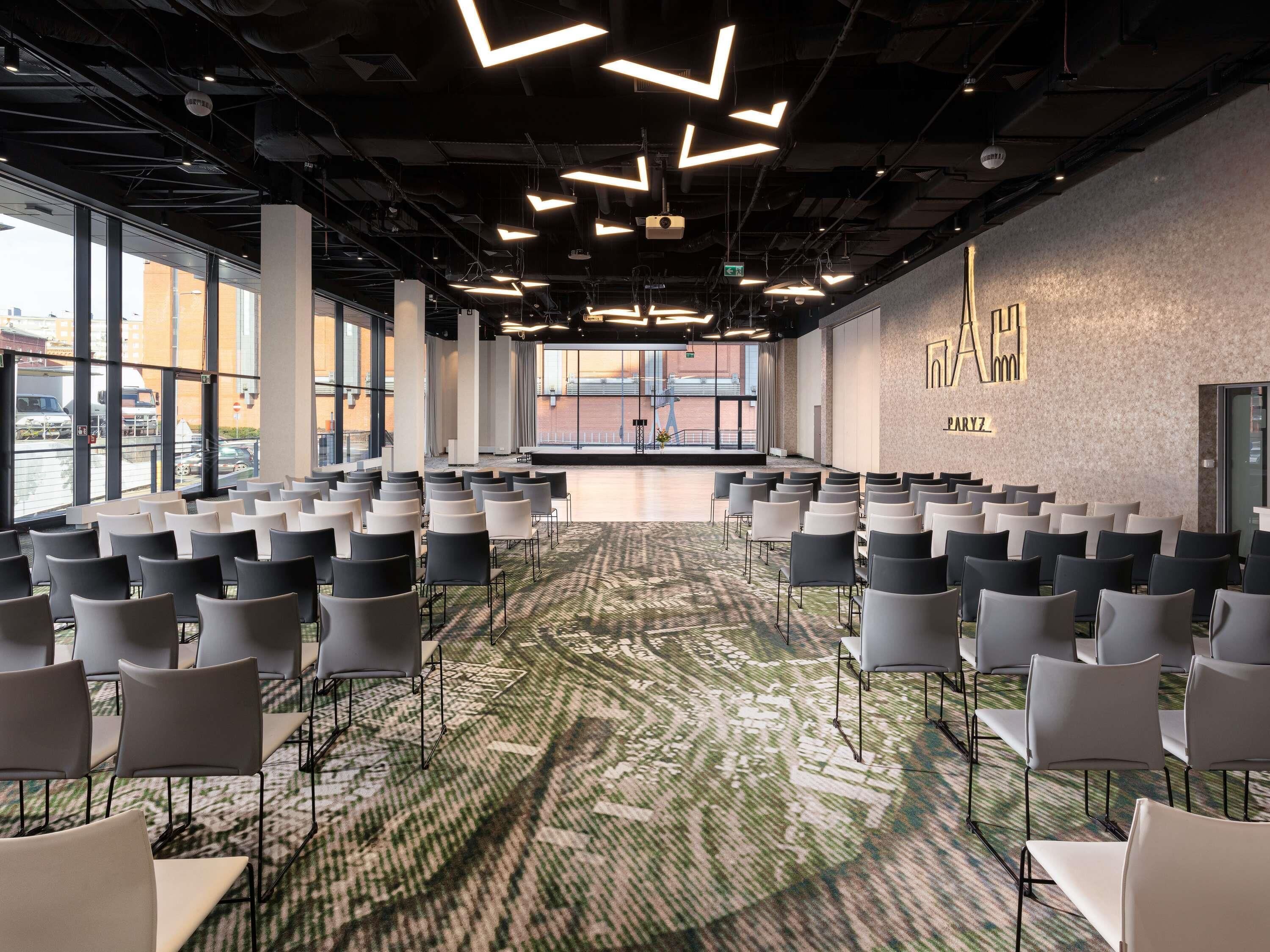 A conference room with rows of chairs, large windows, and a patterned carpet.