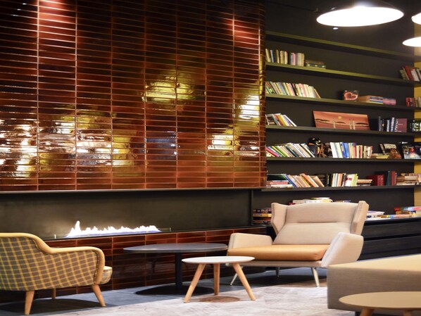 Un espacio lounge moderno con un sillón a cuadros, un sofá, una mesita redonda y una estantería llena de libros.